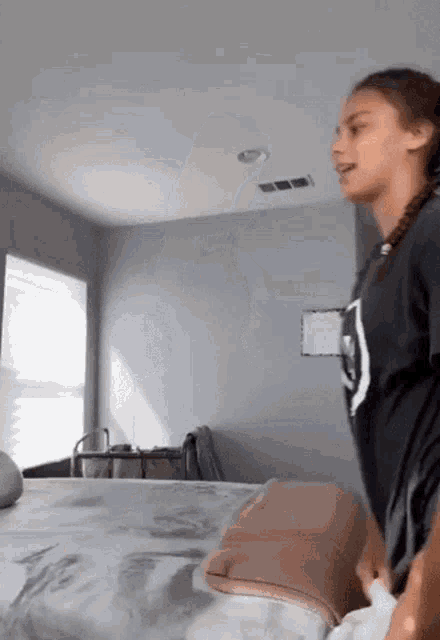 a girl in a black shirt is standing next to a bed in a room .