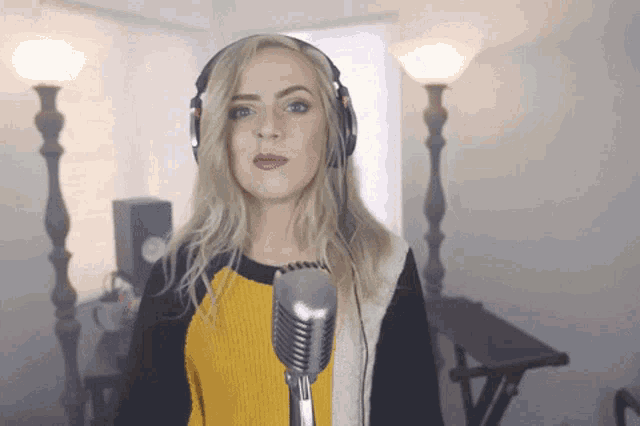 a woman wearing headphones and a yellow and black sweater sings into a microphone