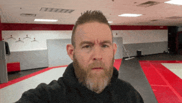 a man with a beard is taking a selfie in an empty gym