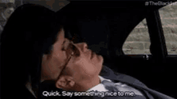 a man and a woman are sitting in a car . the man is wearing sunglasses and the woman is looking at him .