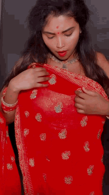 a woman wearing a red saree and a necklace is taking off her blouse .