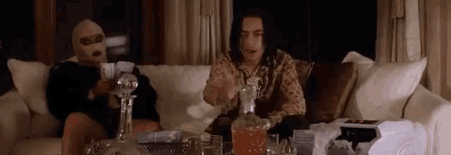 a man and a woman are sitting on a couch with a decanter of alcohol .