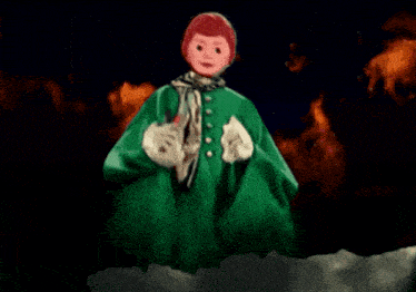 a doll with red hair and a green coat is holding a bag