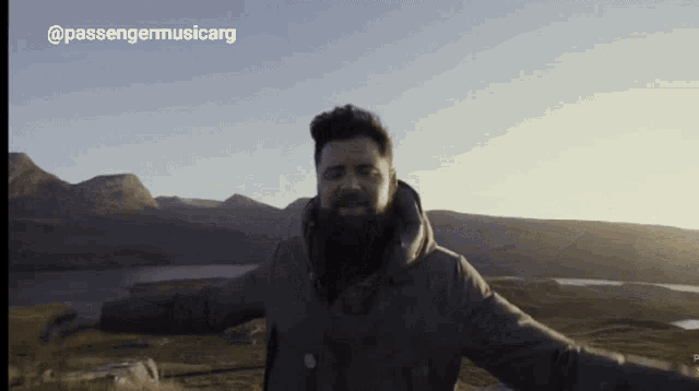 a man with his arms outstretched stands in front of a mountain range with the words passengermusicarg above him