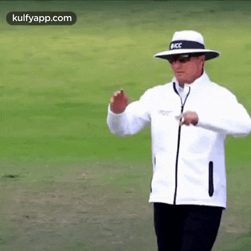 a man wearing a hat and a white jacket is walking on a field .