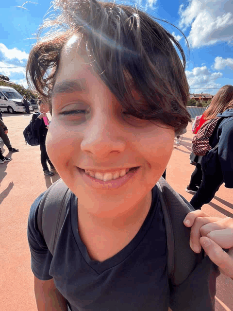 a boy wearing a black shirt and a backpack smiles for the camera