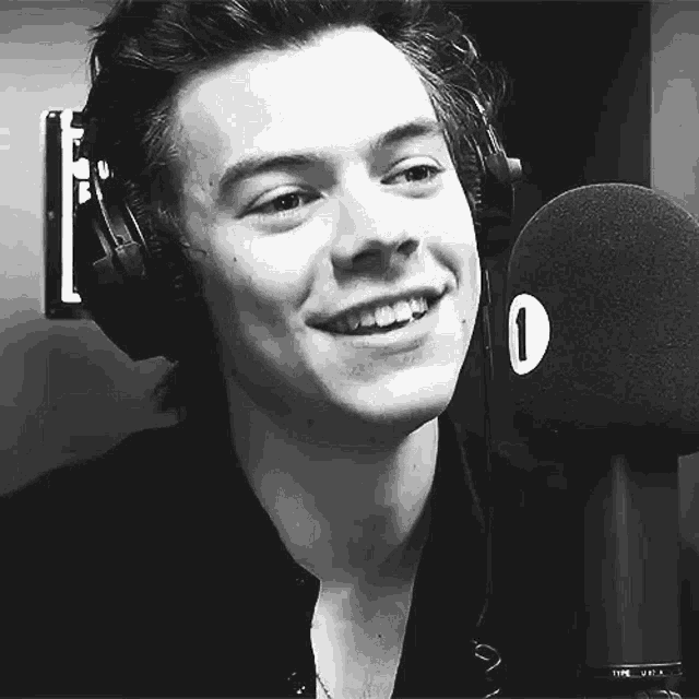 harry styles is wearing headphones and smiling into a microphone .