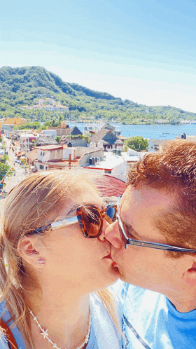 a man and a woman are kissing in front of a mountain