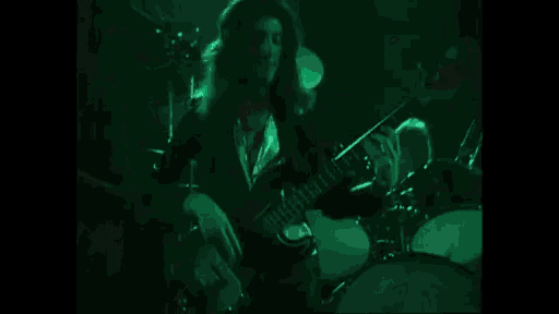 a man is playing a guitar and a drum set on a stage in a dark room .