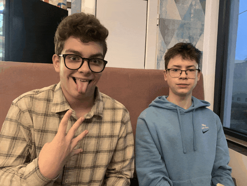 a boy wearing glasses and a blue nike hoodie is sticking his tongue out