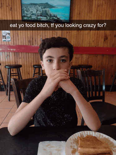a young boy sits at a table with a plate of food and a sign that says eat yo food