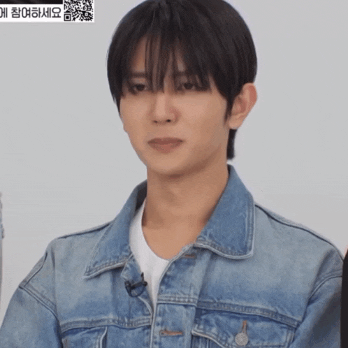 a man wearing a denim jacket and a white shirt looks at the camera