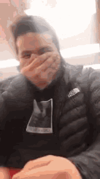 a man wearing a black jacket is covering his mouth with his hand .