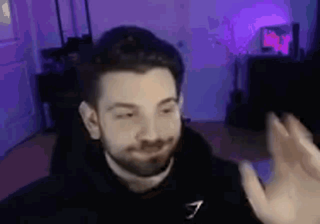 a man with a beard is waving his hand in front of a camera in a room .