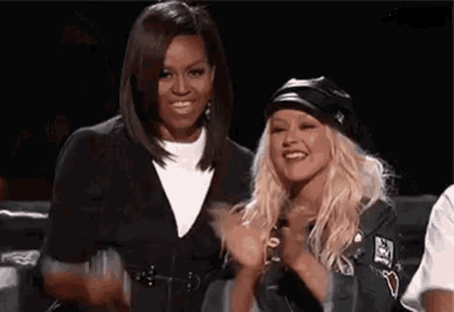 two women are sitting next to each other on a stage and smiling .