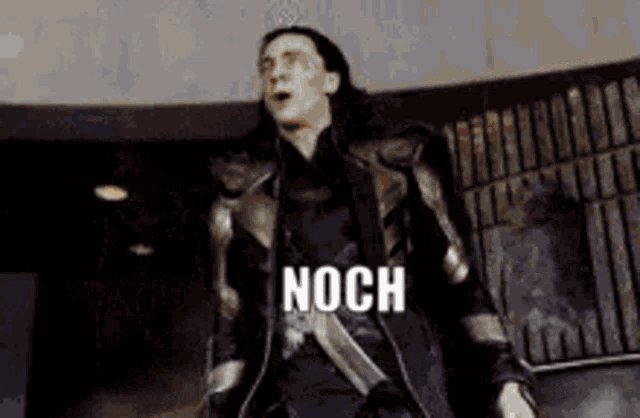 a man in a suit is standing in front of a wall and the word noch is on the screen .