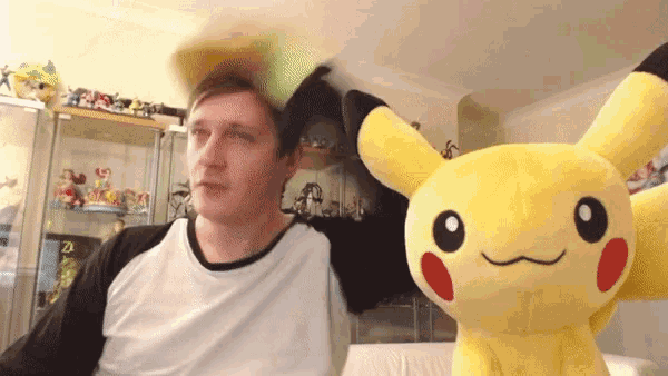 a man in a white shirt is standing next to a pikachu stuffed animal