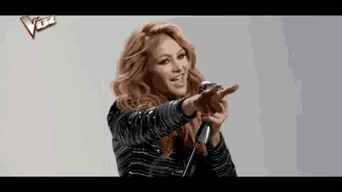 a woman is singing into a microphone and pointing at something .
