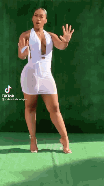 a woman in a white dress and heels is standing on a green carpet .