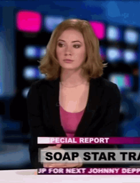 a woman is sitting at a news desk with soap star tra on the screen