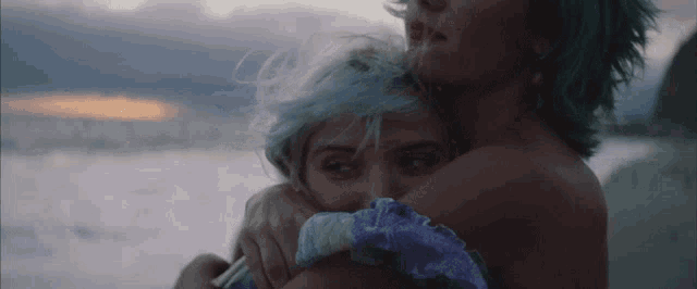 a woman with blue hair is hugging another woman without a shirt