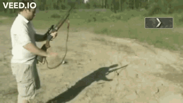 a man is holding a rifle in a field with the website veed.io in the background