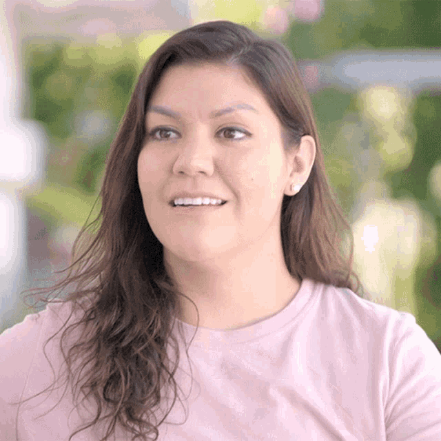 a woman in a pink shirt is smiling and looking away from the camera