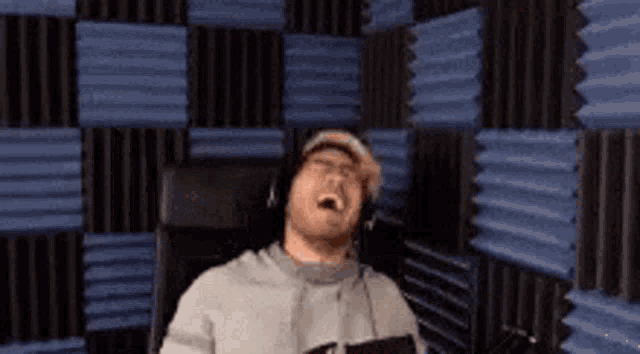 a man wearing headphones is sitting in a chair in front of a microphone in a recording studio .