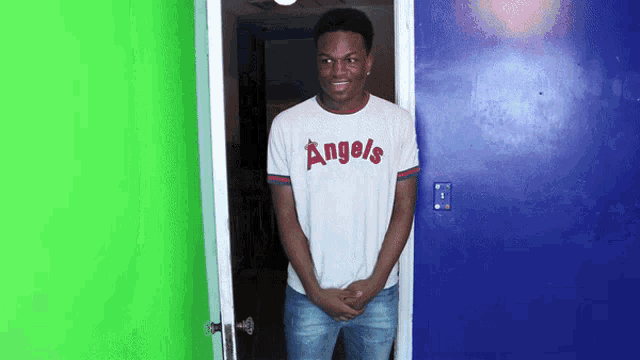a man wearing an angels shirt stands in a blue doorway