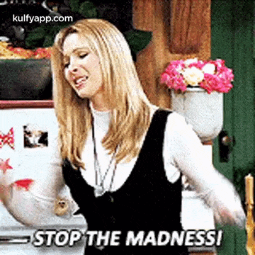a woman is standing in front of a refrigerator with flowers in a vase and says `` stop the madness '' .