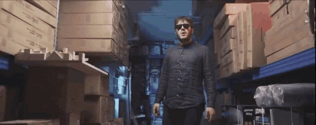 a man wearing sunglasses is walking through a warehouse filled with boxes
