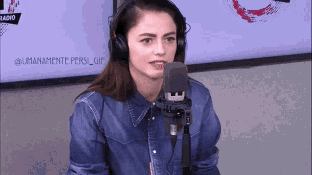 a woman wearing headphones and a denim shirt stands in front of a microphone ..
