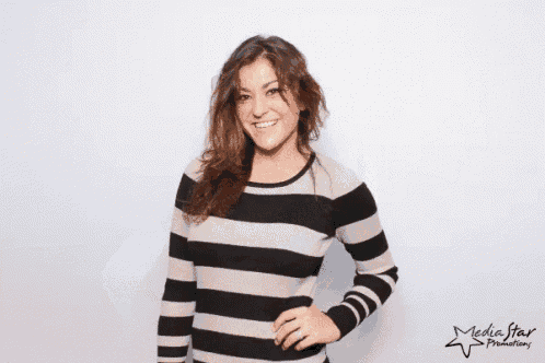 a woman wearing a striped sweater is blowing a kiss in front of a media star advertisement