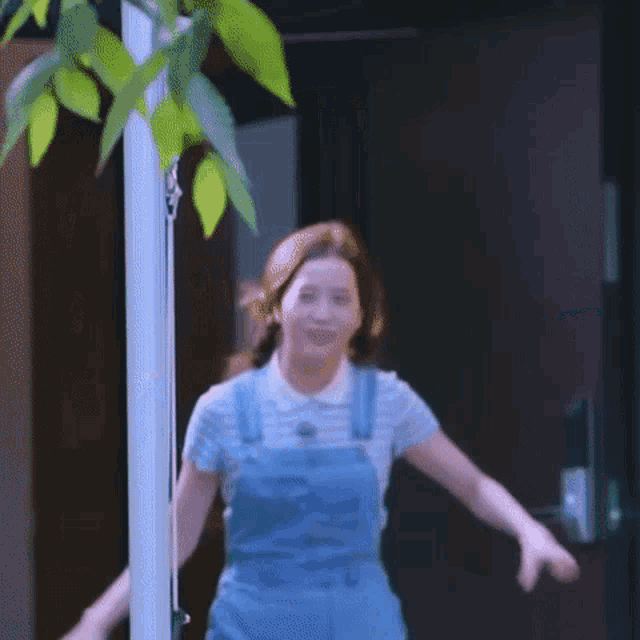 a woman in blue overalls and a white shirt is standing in front of a green door .
