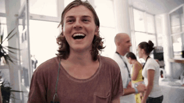 a young man with long hair is laughing in a room with other people