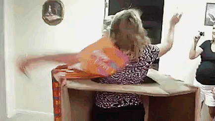 a woman is sitting on an ironing board while another woman takes a picture .