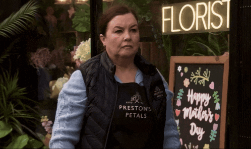a woman wearing an apron that says preston 's petals stands in front of a florist