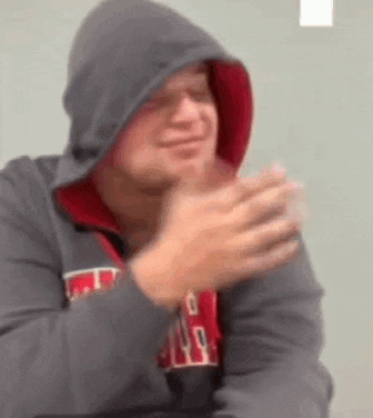 a man in a hoodie is clapping his hands while wearing glasses .