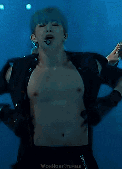a shirtless man with blue hair is standing in front of a microphone with wonhone tumblr written on the bottom right