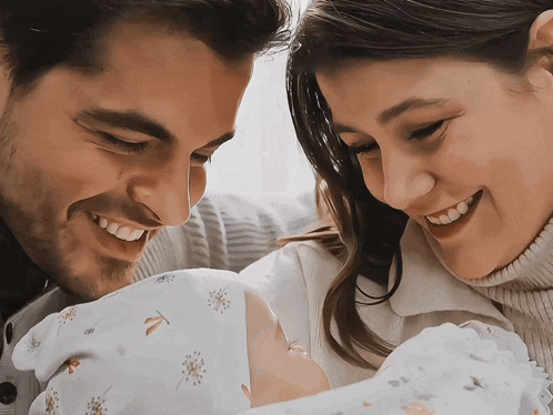 a man and woman are smiling while holding a newborn baby