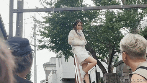a woman in a white dress is standing on a railing with a gifrun.com watermark