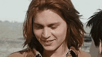 a man with long red hair is smiling with his eyes closed while standing next to another man .
