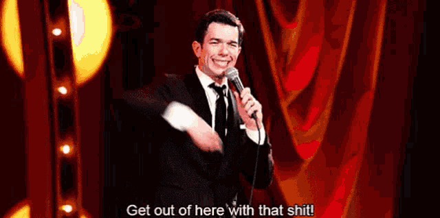 a man in a suit and tie is holding a microphone and saying get out of here with that shit .