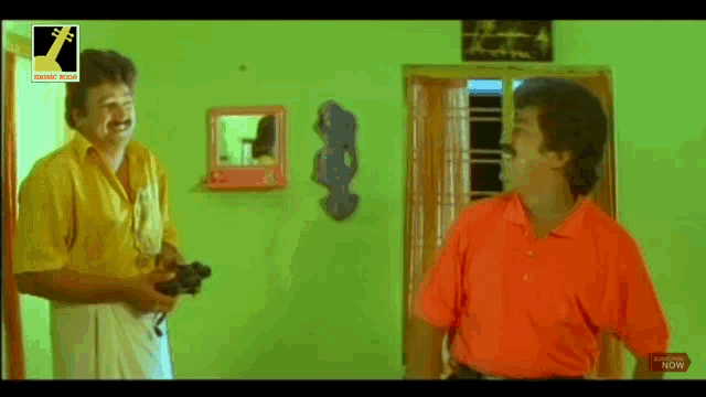 two men are standing next to each other in a room and talking to each other .