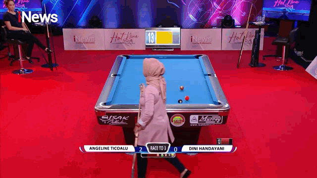 a woman in a hijab is playing pool in front of a screen that says inews