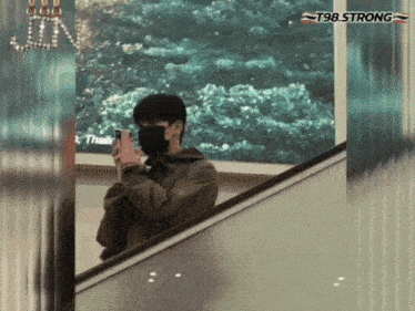 a man wearing a mask is standing on an escalator and looking at his cell phone