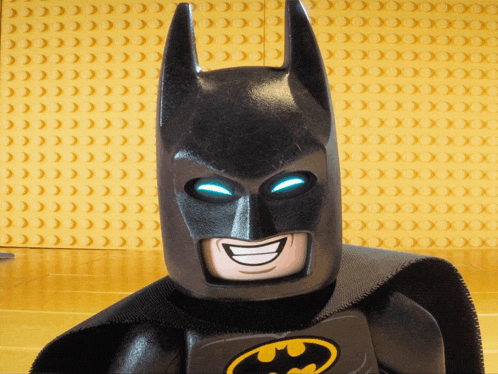 a lego batman is smiling in front of a wall of yellow bricks