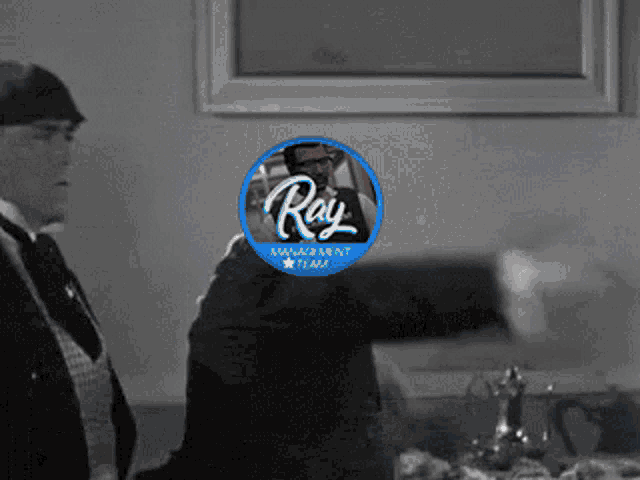 a man in a suit and tie is standing in front of a window with a ray management team logo
