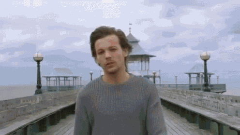a man in a sweater is standing on a pier looking at the camera .