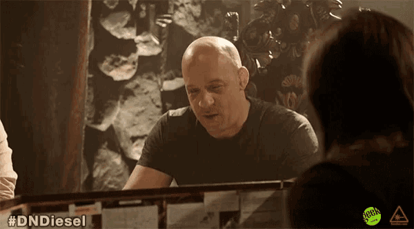 a bald man in a black shirt is talking to a woman with #dnddiesel written on the bottom